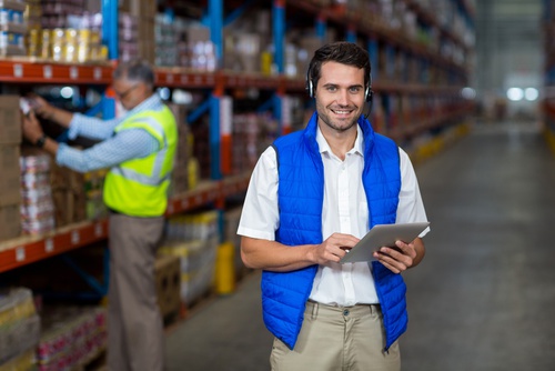 Standing worker smiling at camera while holding digital tablet